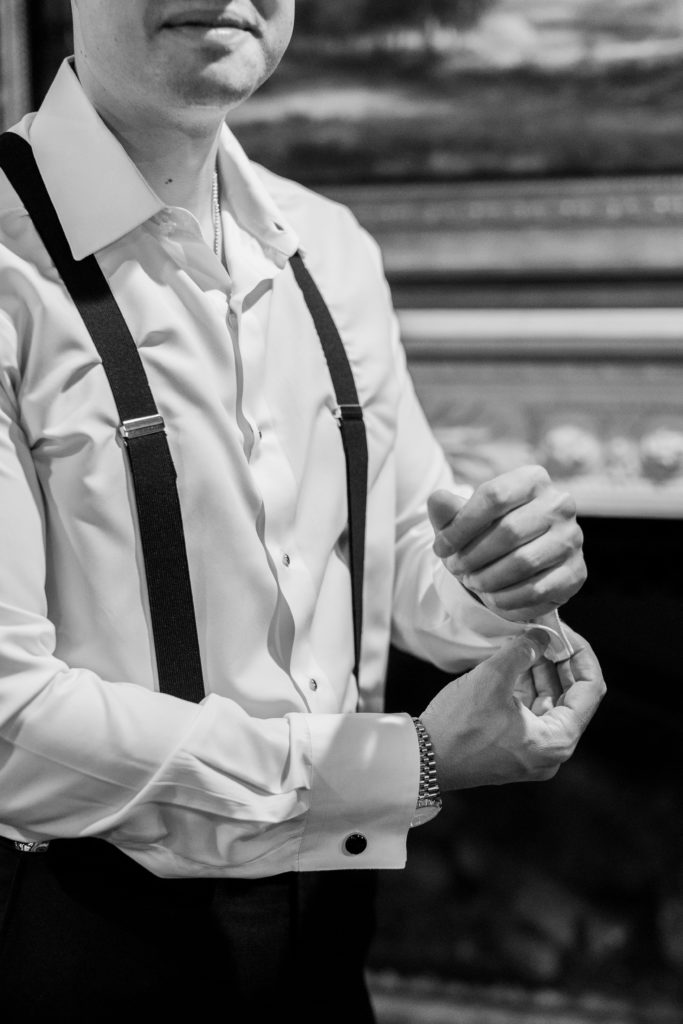 groom buttoning sleeve before wedding ceremony in black and white