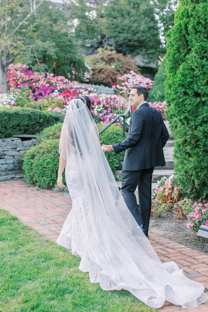 bride and groom walk through garden with long train behind them - Park Savoy Wedding Photography