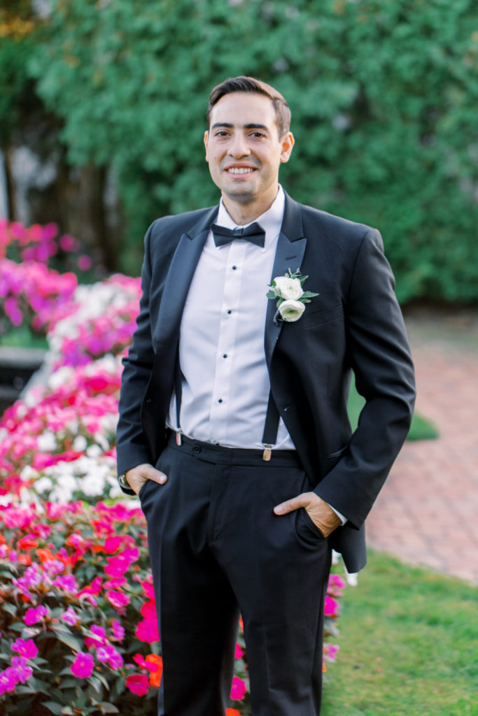 Groom stands in the garden with hands in pockets