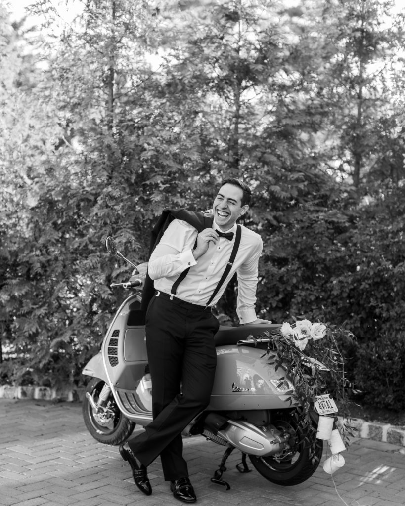 groom laughs as he leans on decorated vespa - Park Savoy Wedding Photography