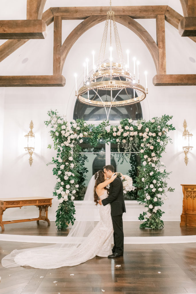 bride and groom kiss in chapel under flower filled arch