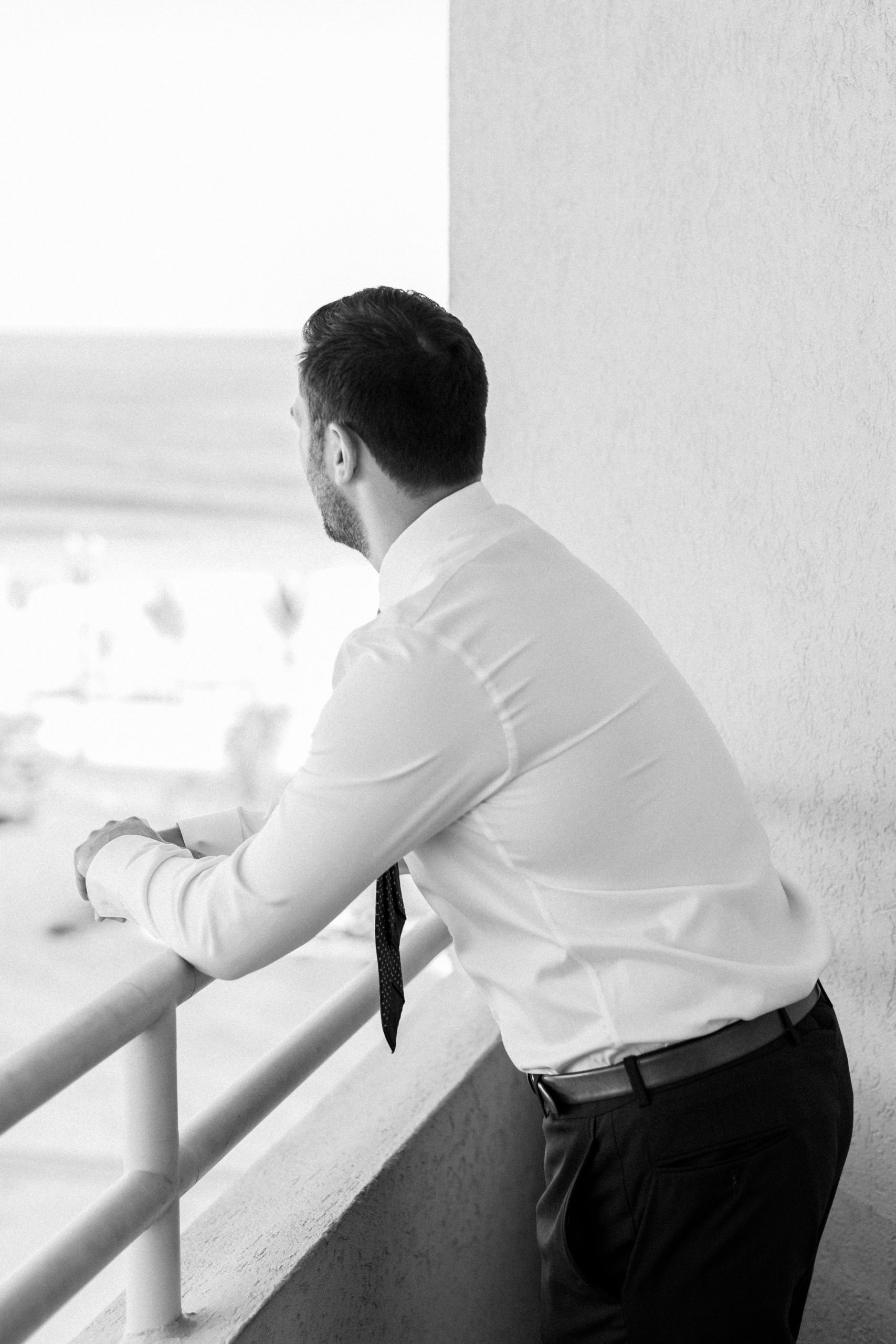 groom looks out at ocean from balcony in black and white NJ Private Estate Wedding Photography