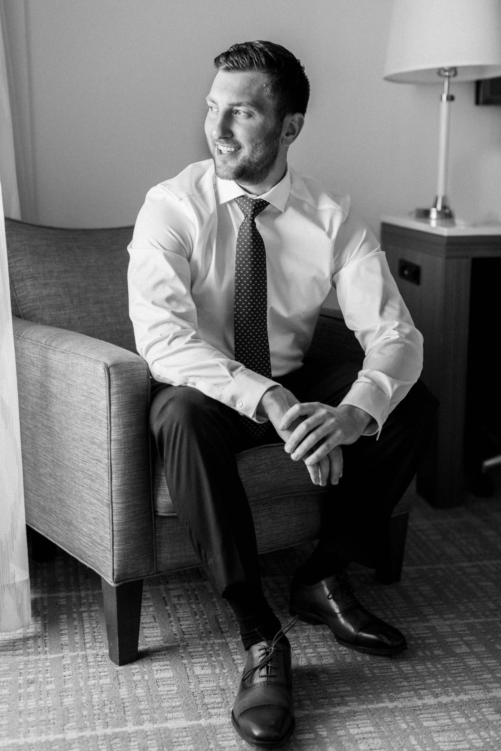 groom smiles as he lounges in chair in black and white NJ Private Estate Wedding Photography