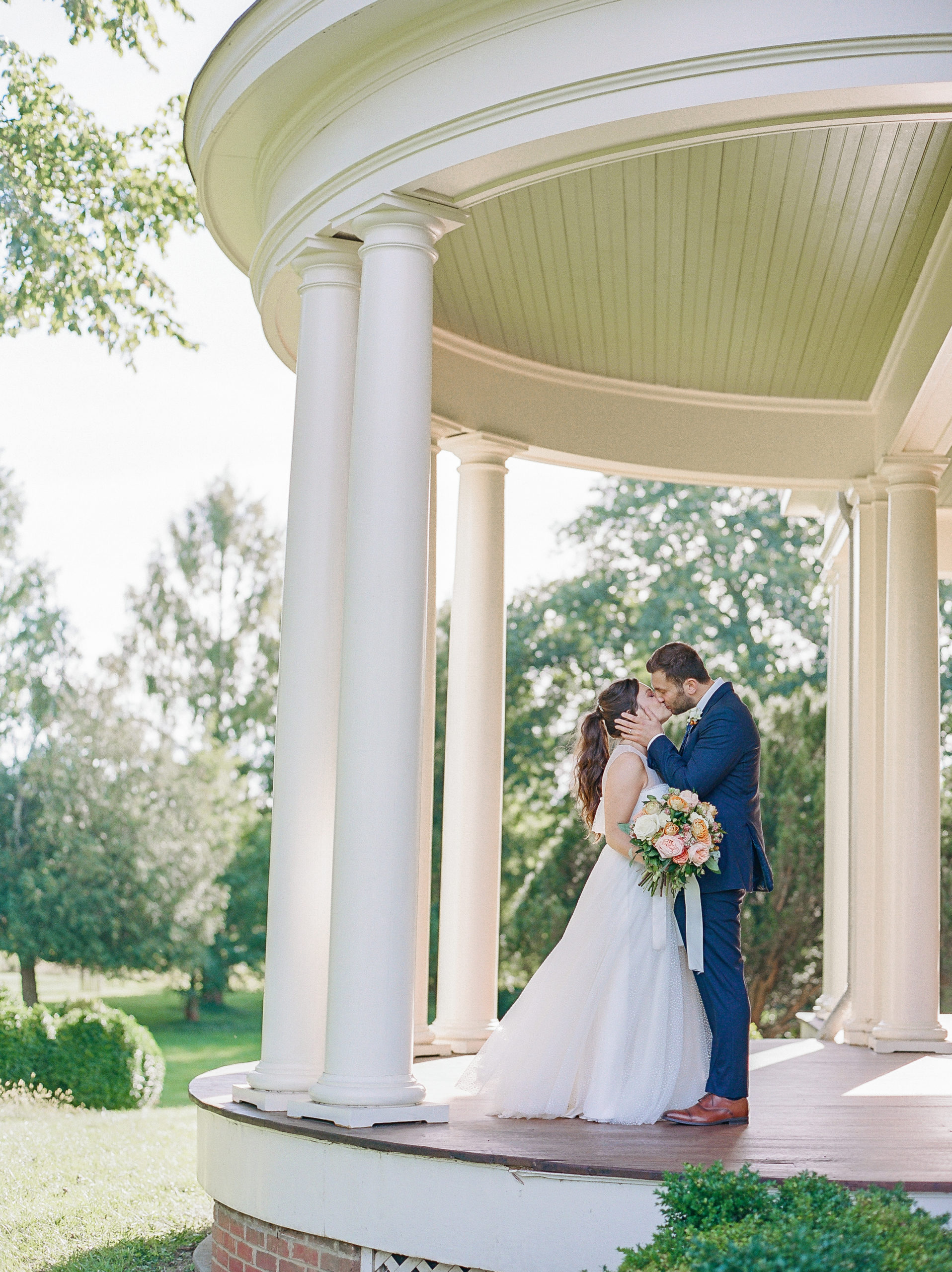 Bride and groom kiss on rotunda porch surrounded by treesNJ Private Estate Wedding Photography
