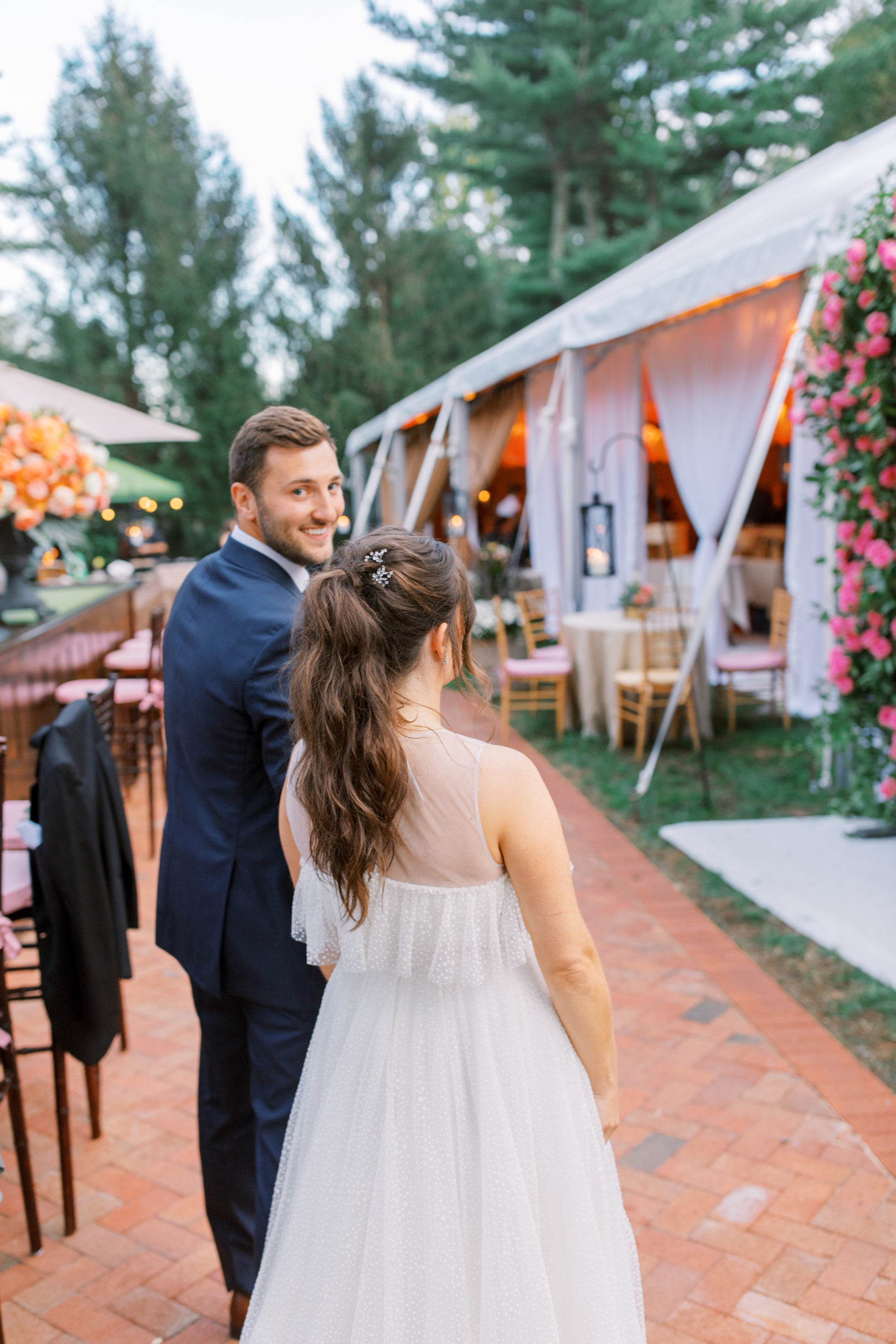 groom smiles back as he and bride wait to enter reception tent amid roses and trees NJ Private Estate Wedding Photography