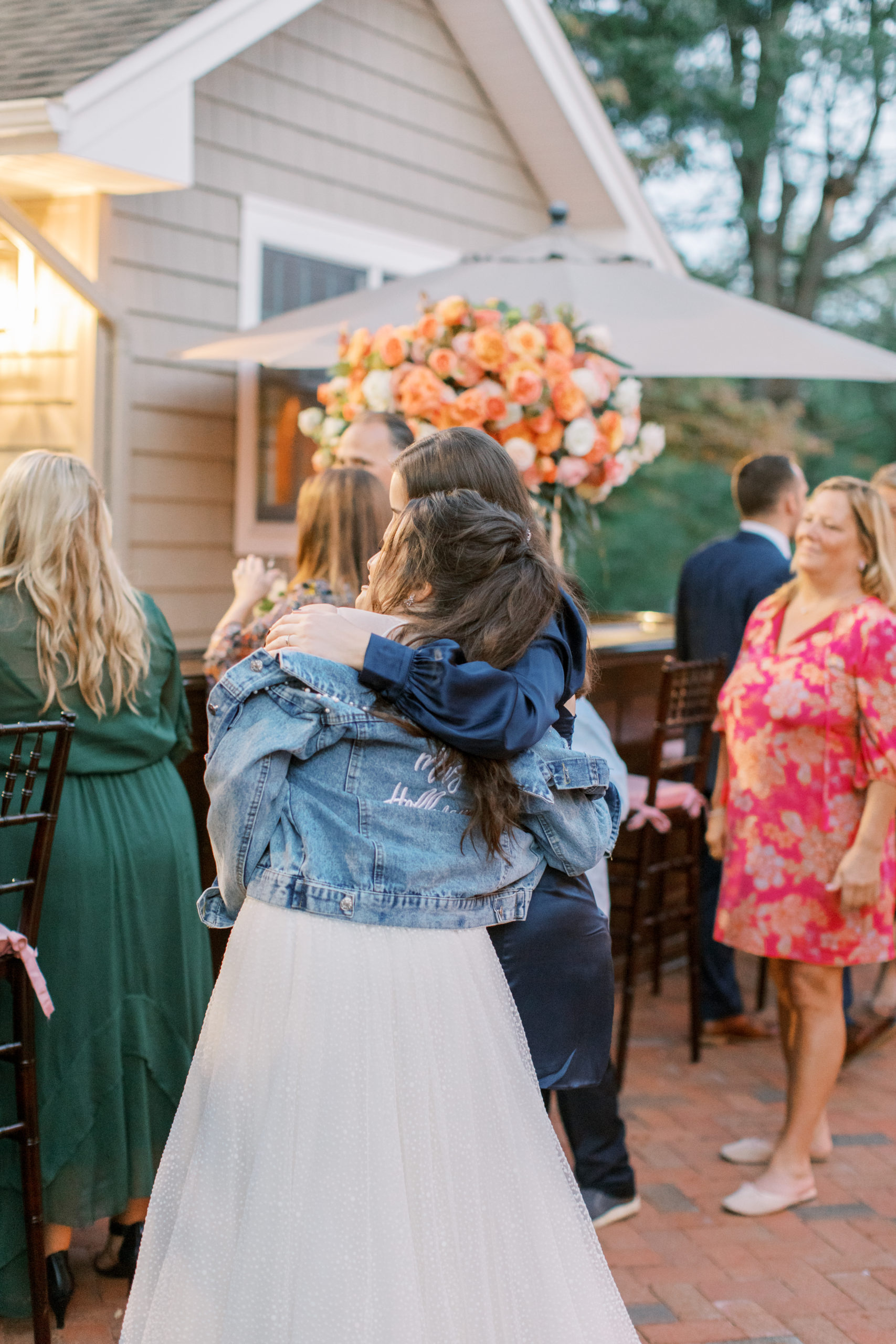 bride in custom jean jacket embraces friend during cocktail hour NJ Private Estate Wedding Photography