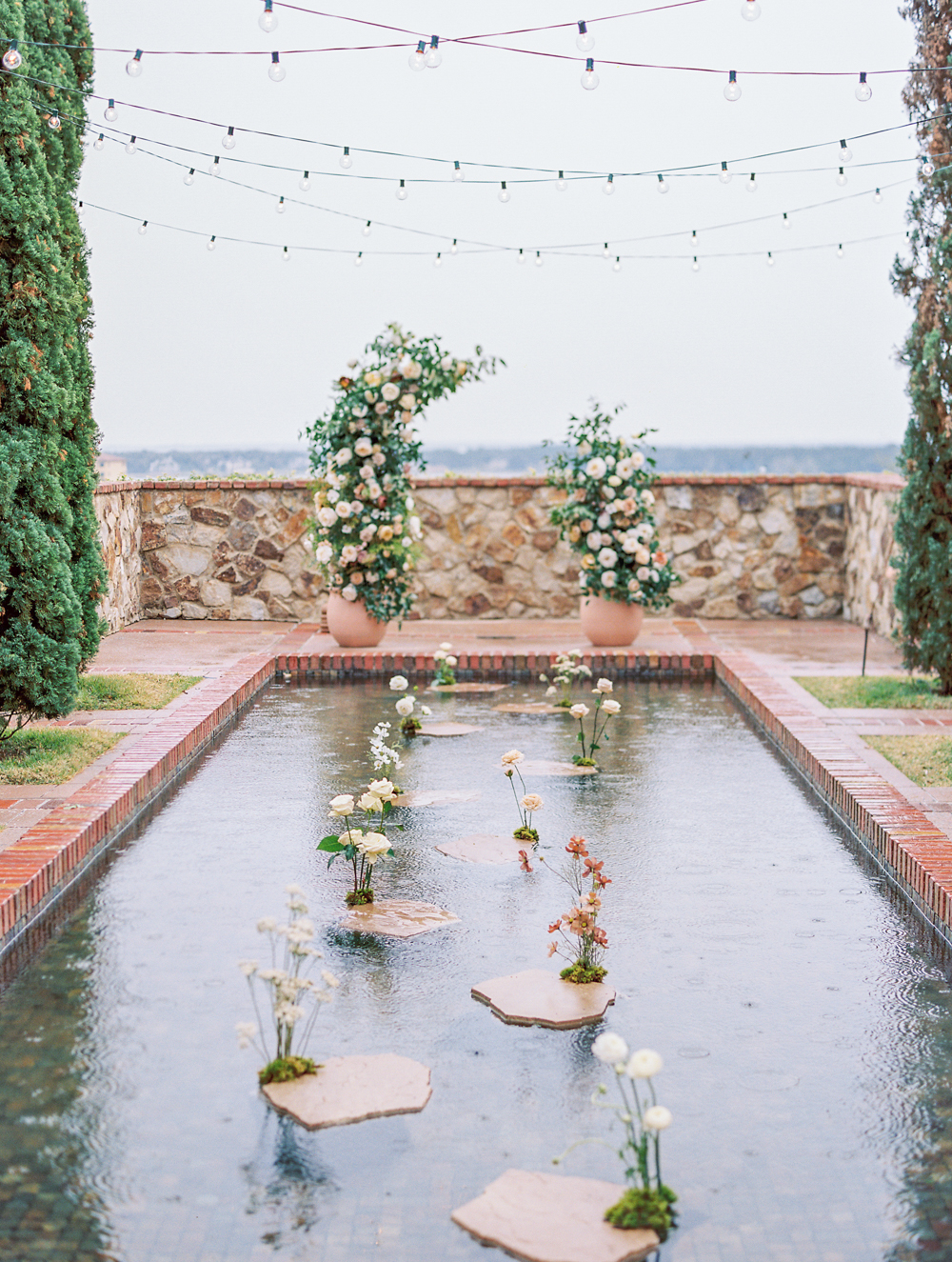 luxurious floral wedding arch in front of reflecting pool on rainy day