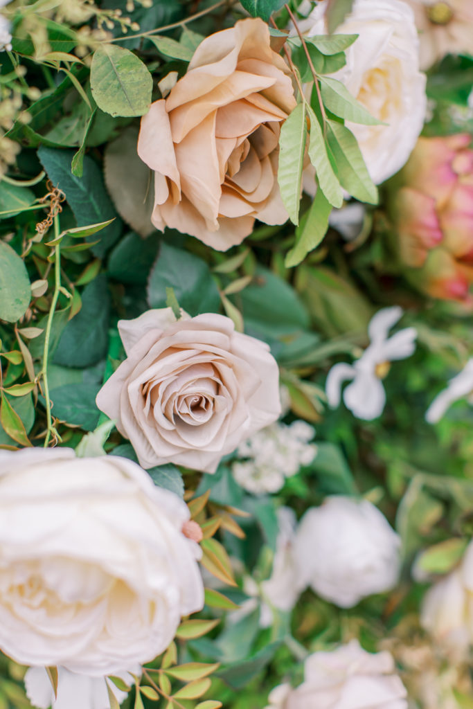 close up detail of ivory and honey colored roses amid greenery Bella Collina Wedding