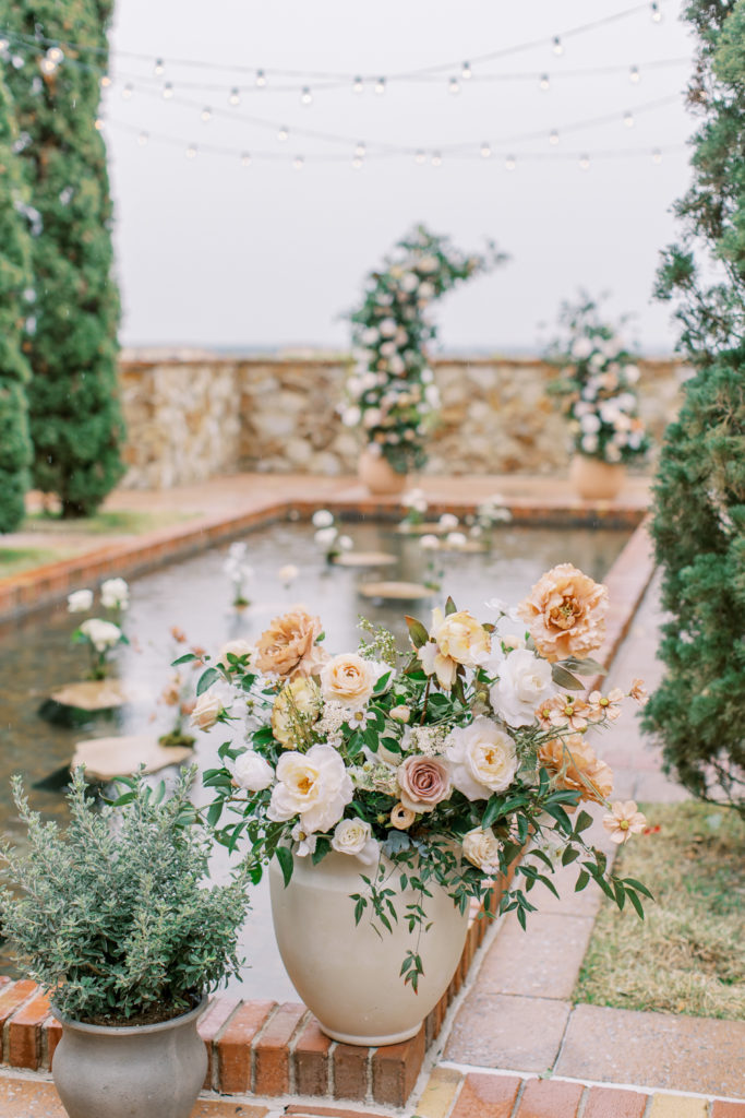 potted floral arrangement in front of reflecting pool with floral arch in the background