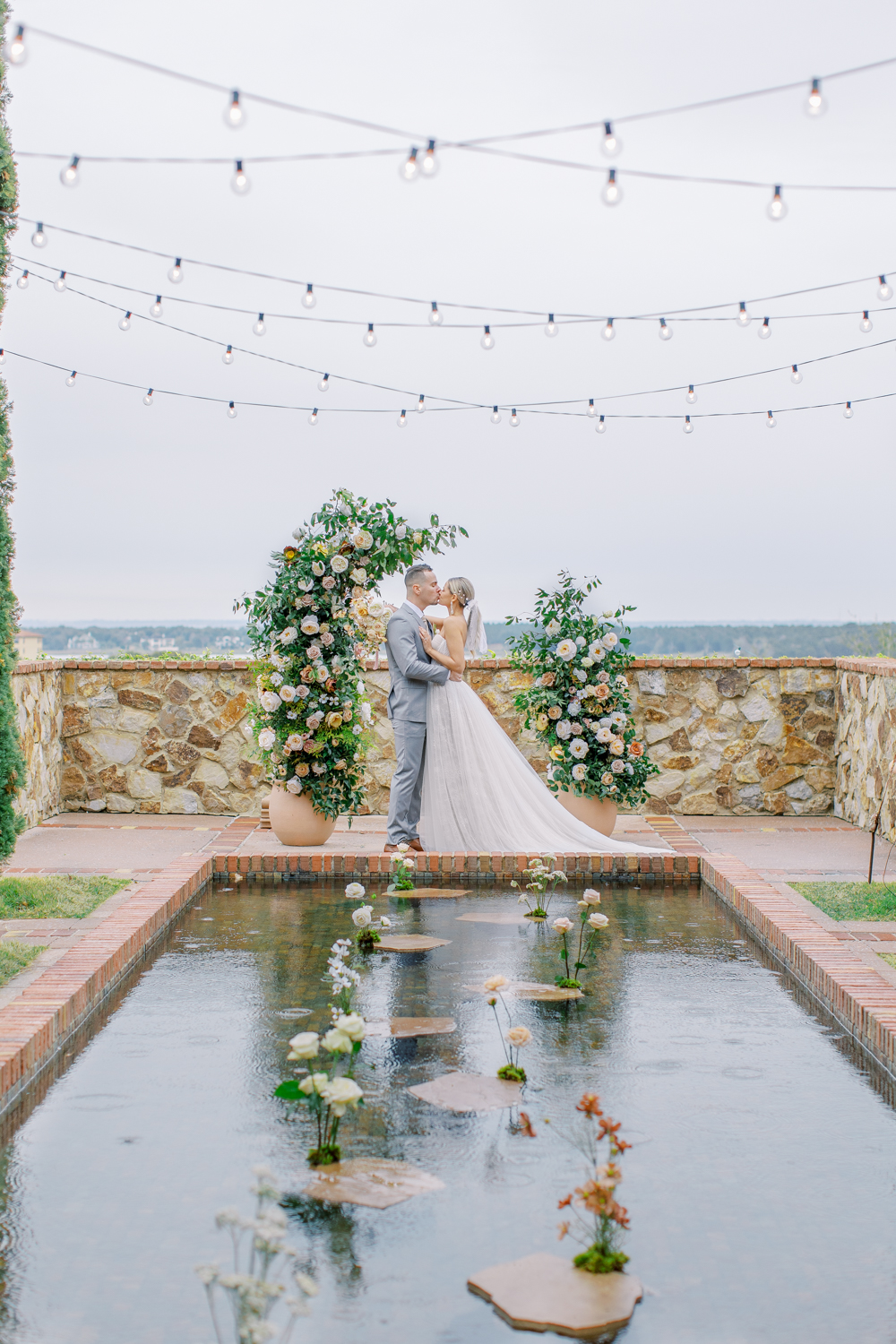 bride and groom kiss in front of reflecting pool with large floral arch Bella Collina Wedding