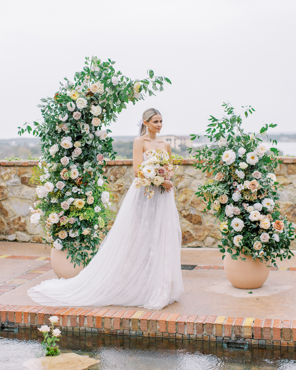 bride stands in front of large floral arch holding blush bouquet Bella Collina Wedding