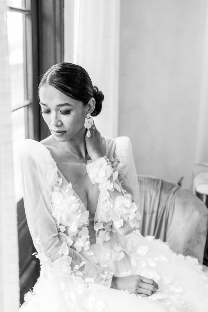 bride sits by window getting ready for wedding in black and white