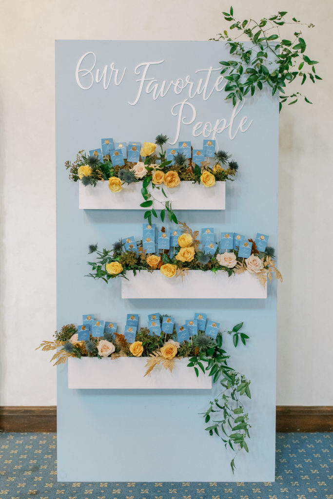 blue seating assignment sign with boxes of gold and cream roses