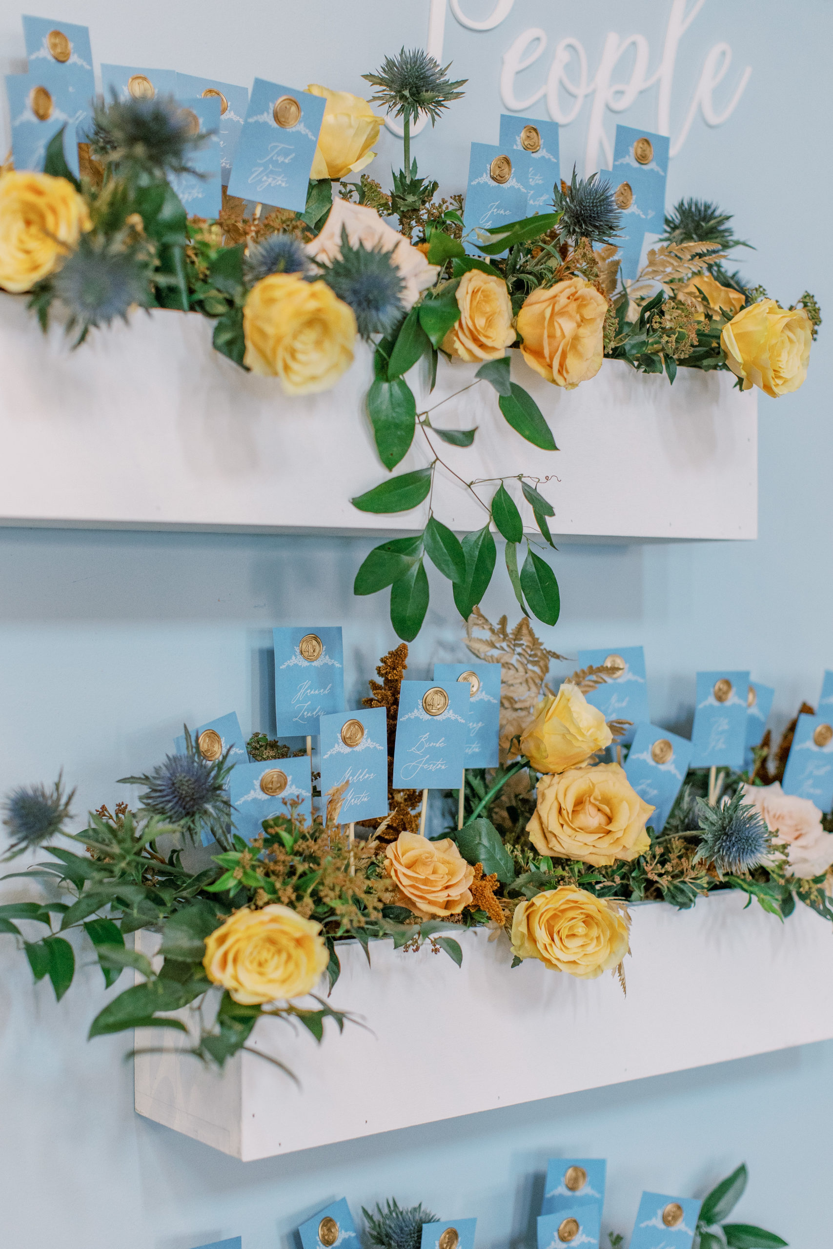boxes of gold roses with seating chart cards interspersed with greenery Bella Collina Wedding Photography