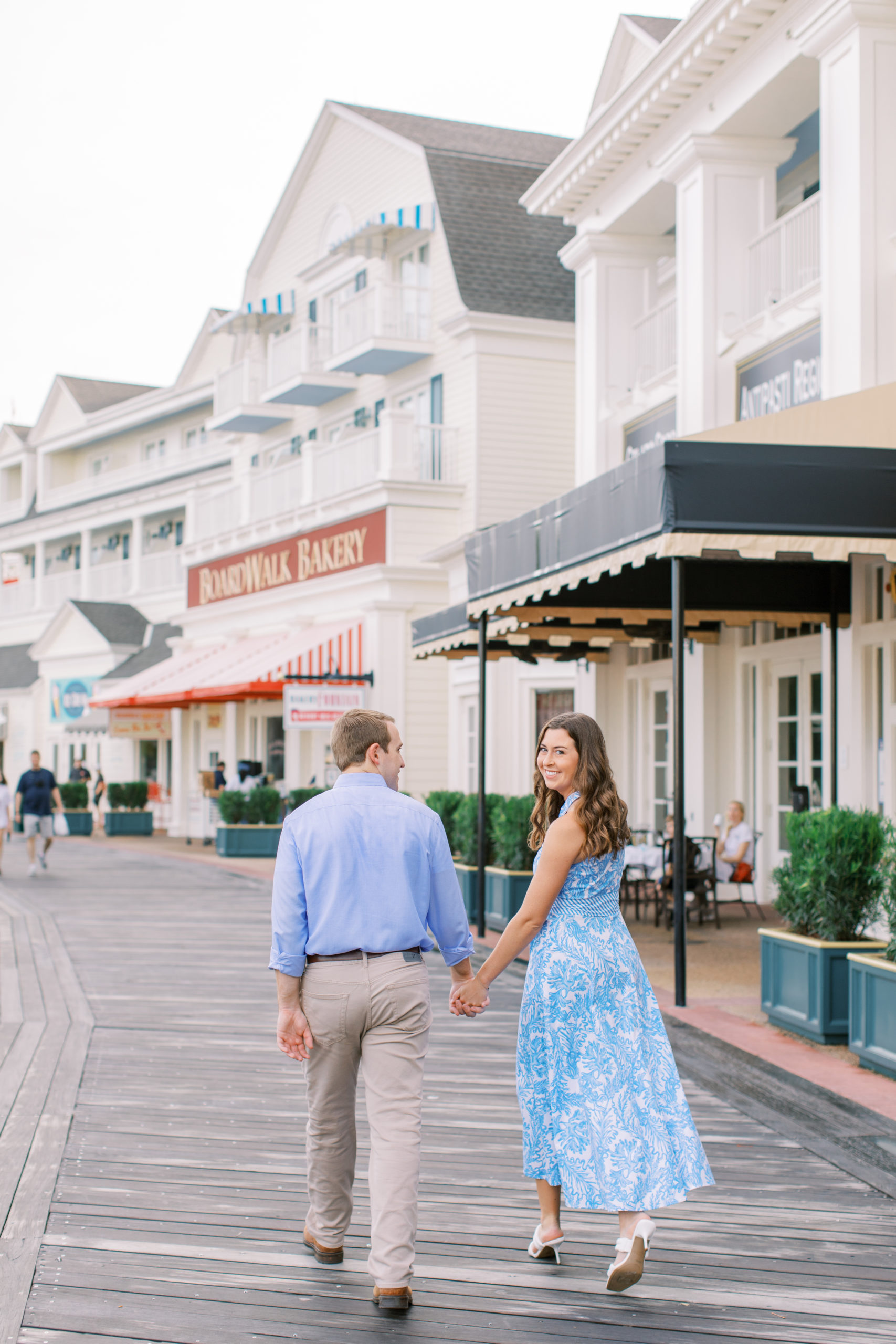 Couple dressed in blue walk hand in hand at Disney's Boardwalk Engagement Session