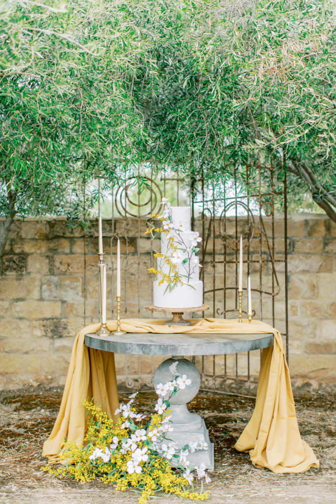 wedding cake with gold flowers surrounded by olive trees