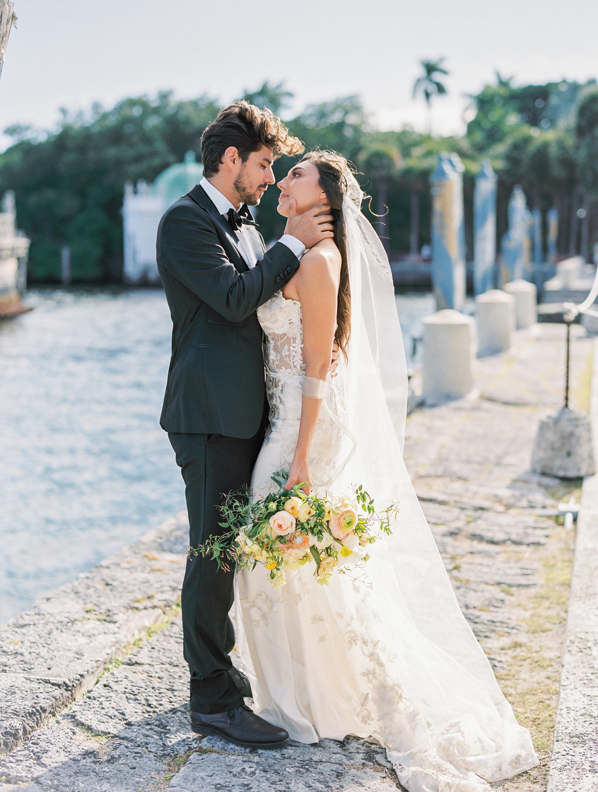 bride and groom embrace at waterfront of vizcaya museum