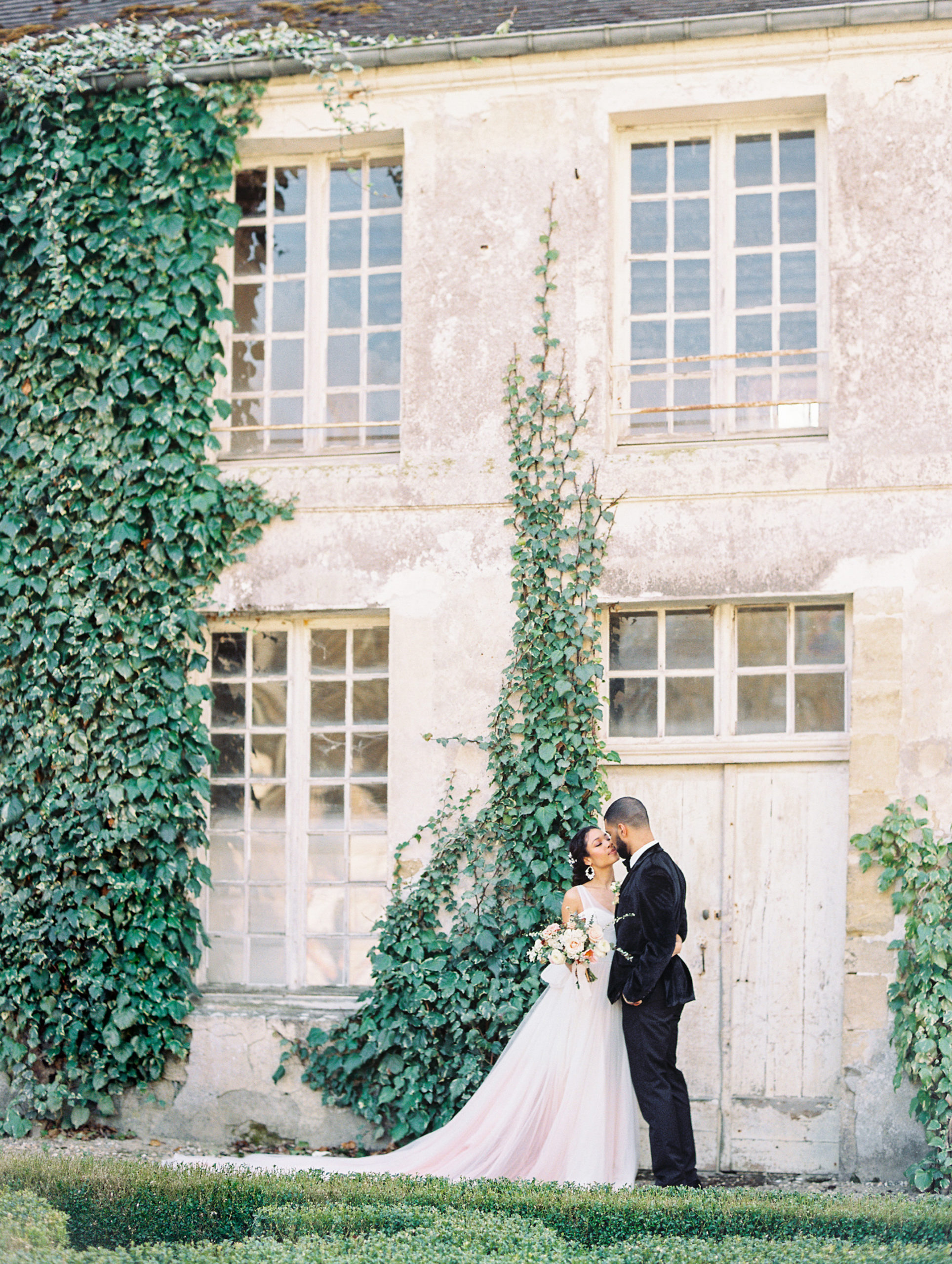 Bride and groom kiss in front of vine wall and stone estate at Chateau de Villette Wedding Photography