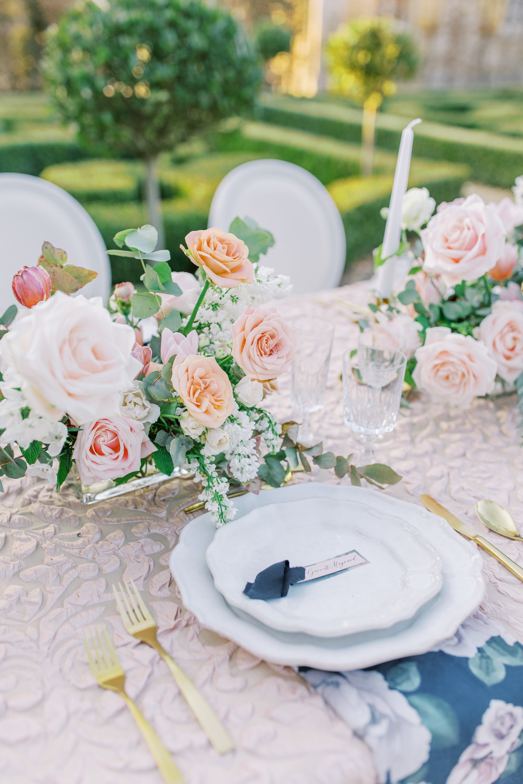 Wedding reception table setting with cream, orange, and pink roses and gold utensils 