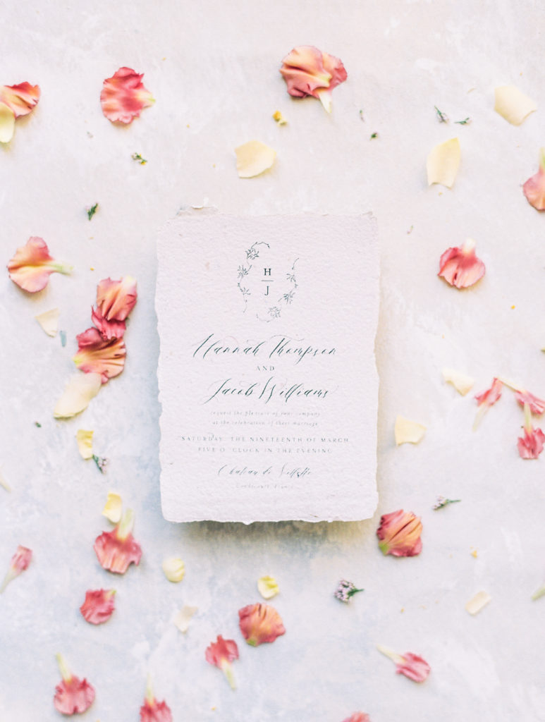 Wedding invitation with pink and cream rose petals and delicate calligraphy 