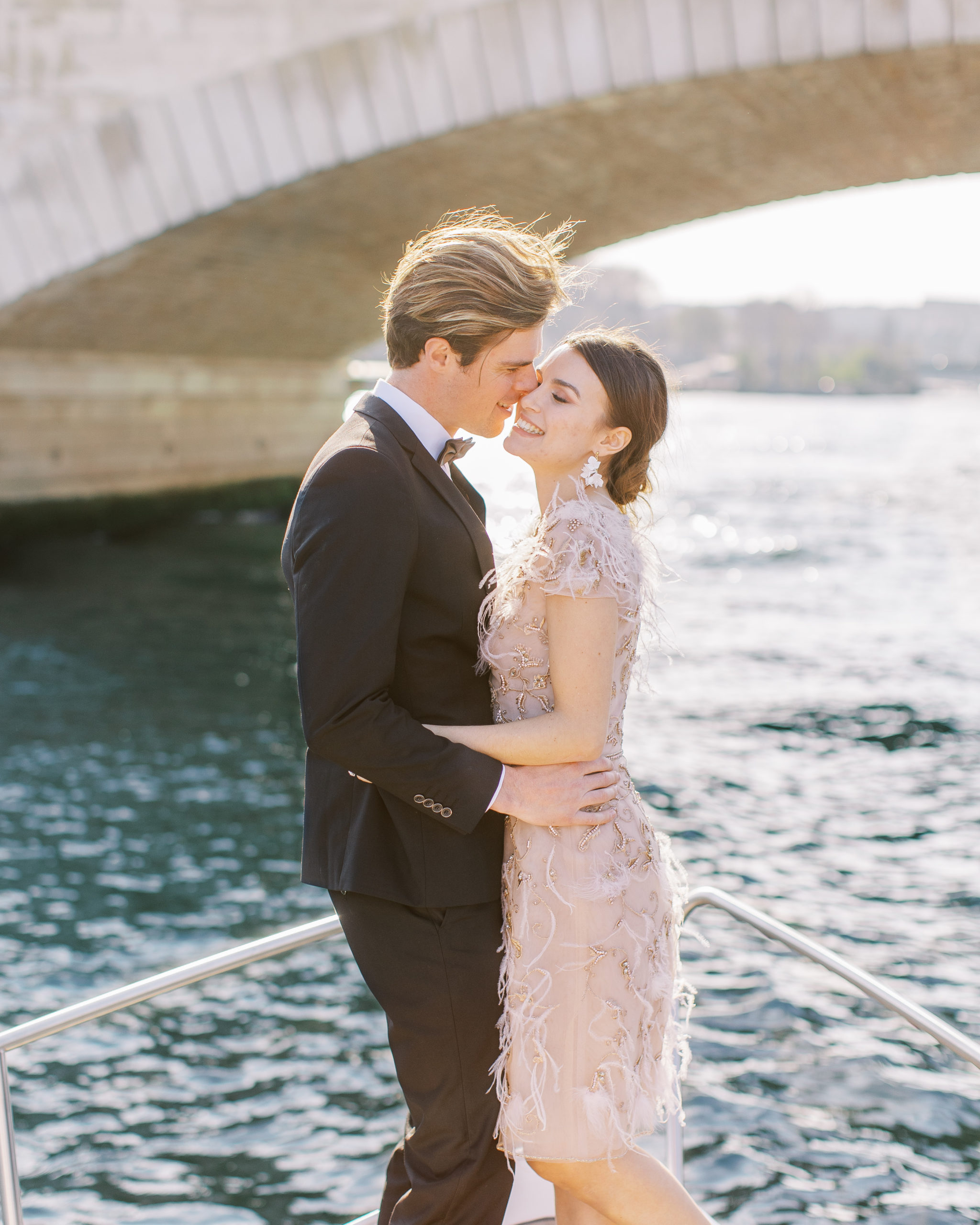 Couple embracing and smiling on boat going underneath bridge for Sunset Paris Engagement 