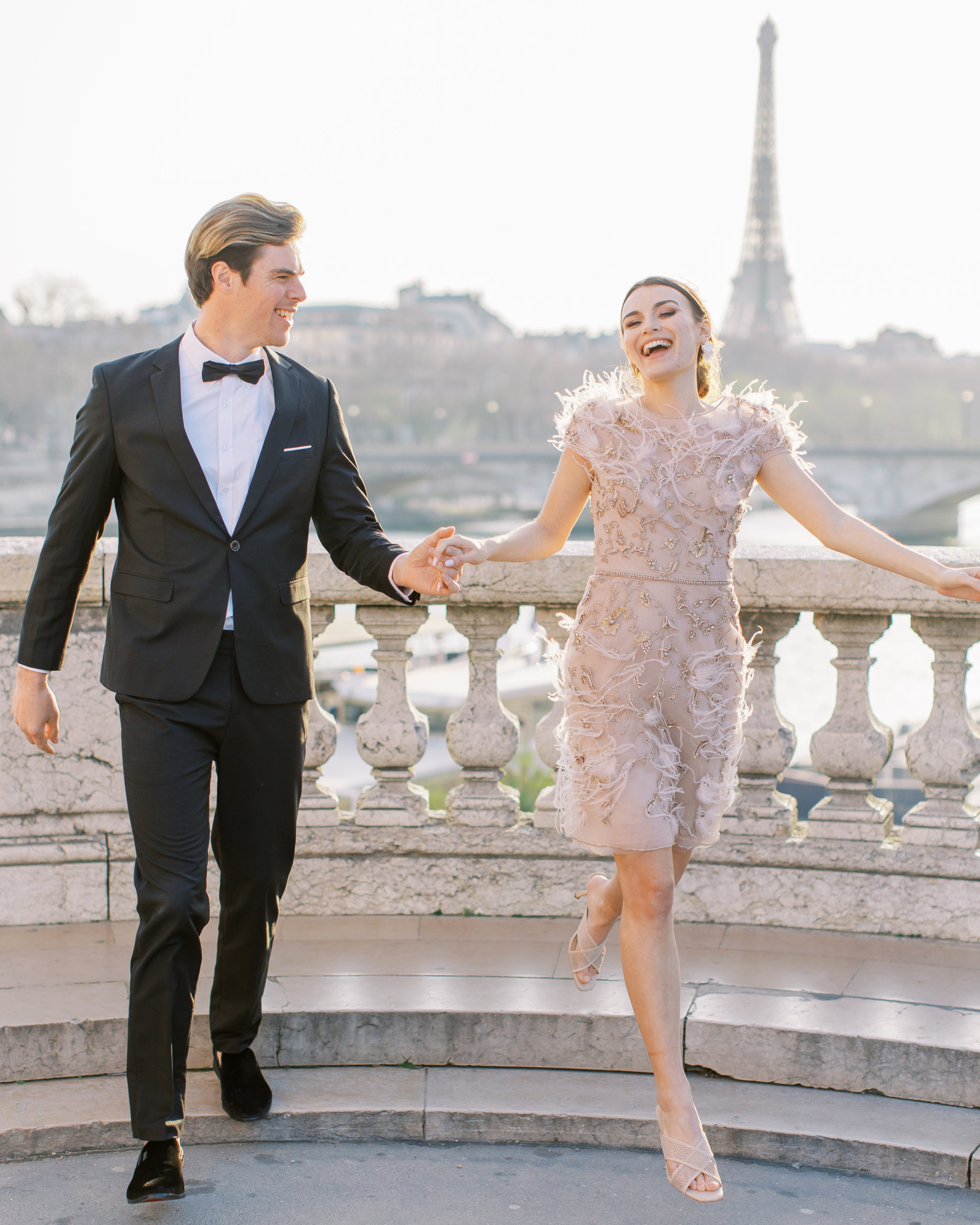Couple holding hands, smiling, walking off steps with Eiffel Tower in background 