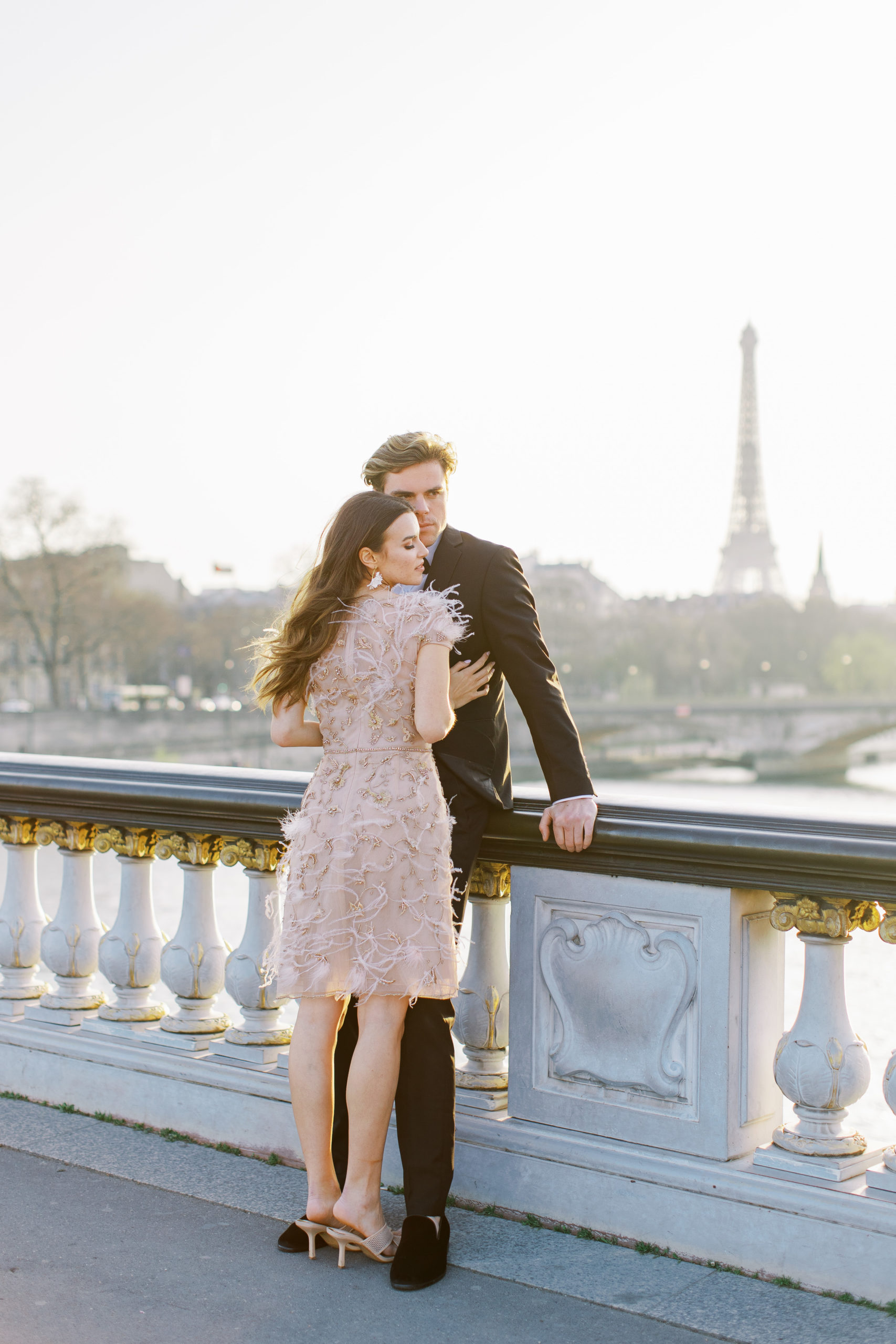Couple embracing against bridge with Eiffel Tower in background for Sunset Paris Engagement 