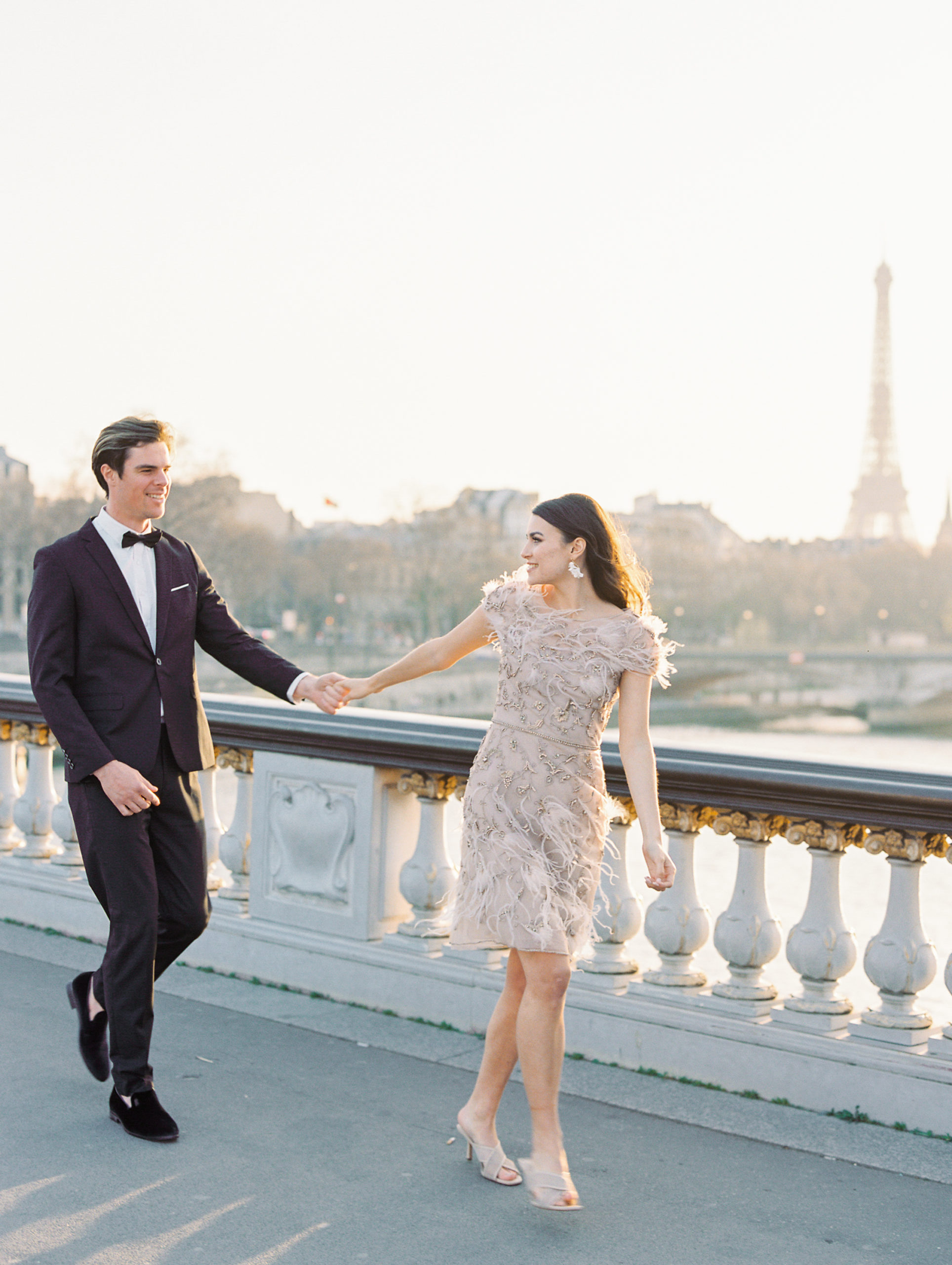 Couple holding hands looking at each other on bridge with Eiffel Tower in background 