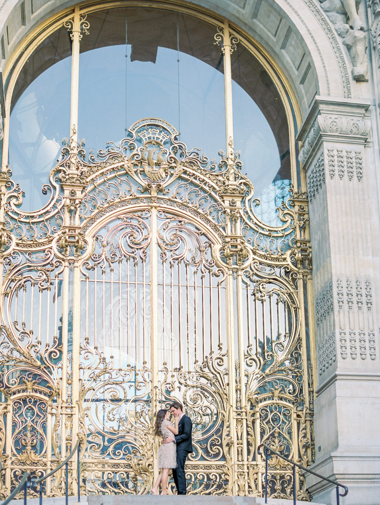 Couple embrace in front of golden gates for Sunset Paris Engagement 
