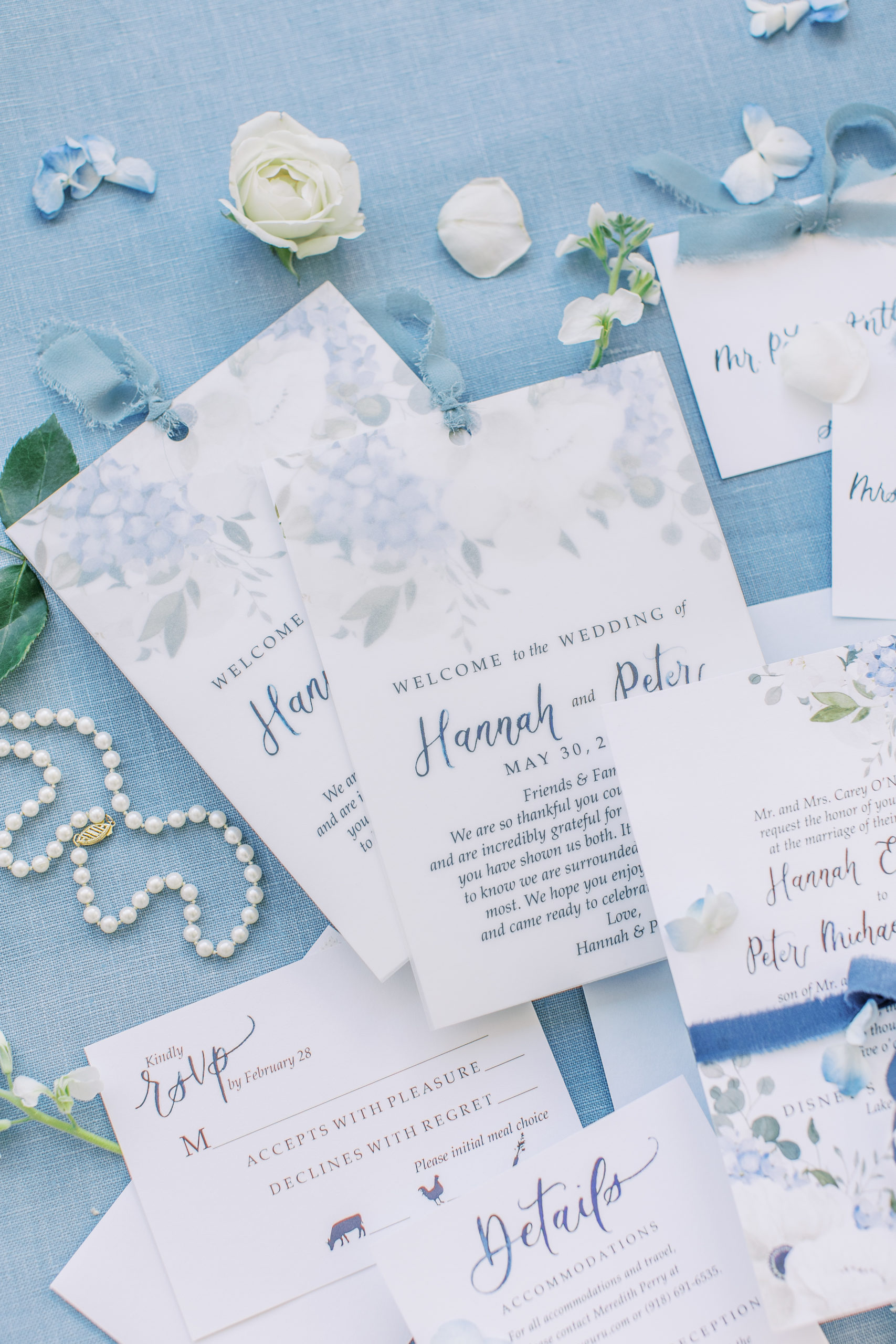 Detailed view of light blue wedding invitations with white and blue flowers and pearl necklace 