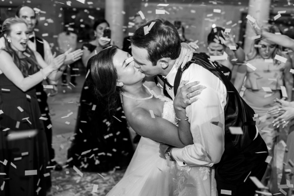 Bride and groom kiss on dance floor as confetti falls 