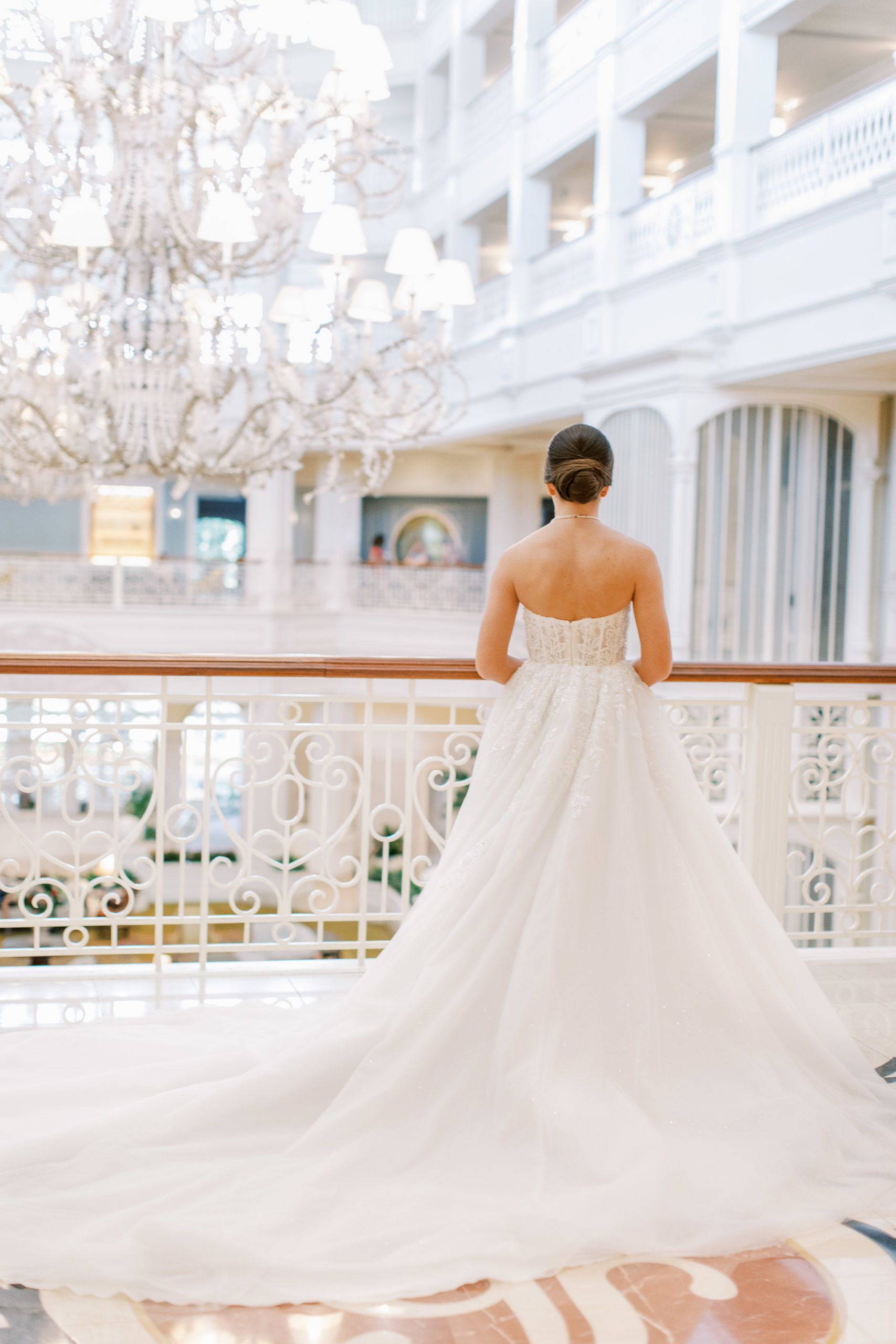 Bride stands away with detailed railing and large chandelier with her dress flowing behind 
