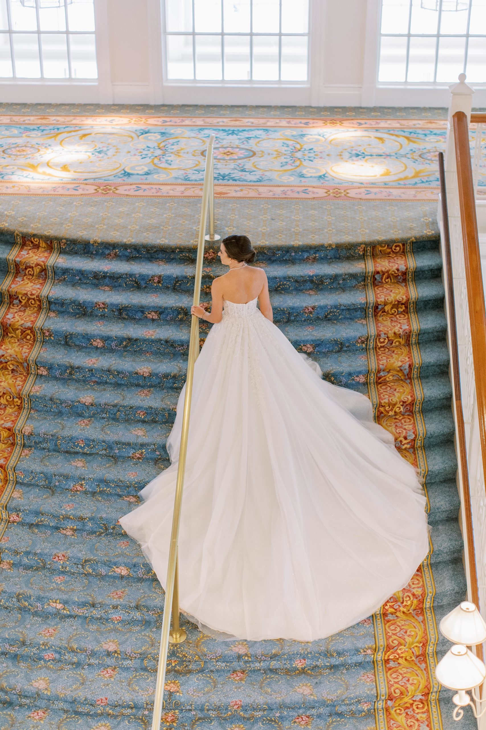 Bride walks up grand staircase holding onto gold rail 