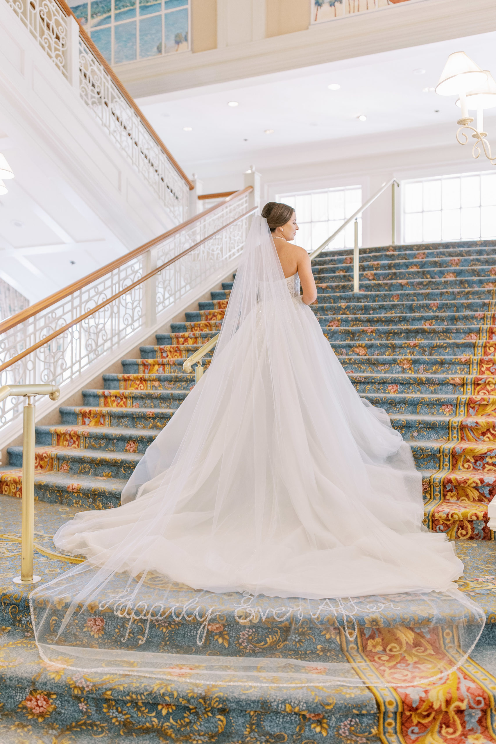 Bride walks up grand staircase as her dress flows down the stairs with vail saying "Happily Ever After" for a Romantic and Timeless Grand Floridian Wedding 