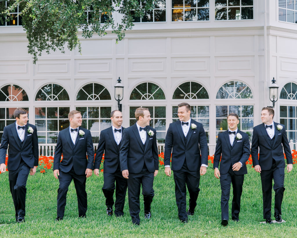 Groom and groomsmen smile and walk in grass for a Romantic and Timeless Grand Floridian Wedding 