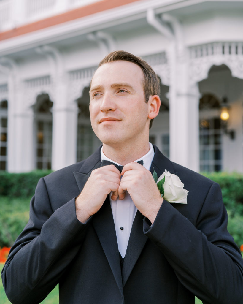 Groom in black suit adjusts bowtie for a Romantic and Timeless Grand Floridian Wedding 