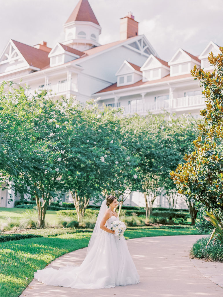 Bride holds bouquet in pathway outside of Disney resort at a Romantic and Timeless Grand Floridian Wedding 