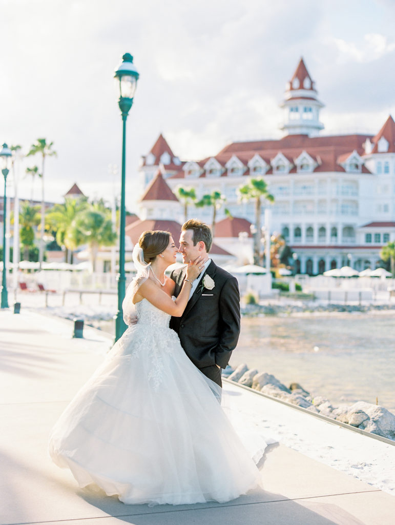 Bride and groom smile and embrace alongside small lake at a Romantic and Timeless Grand Floridian Wedding 