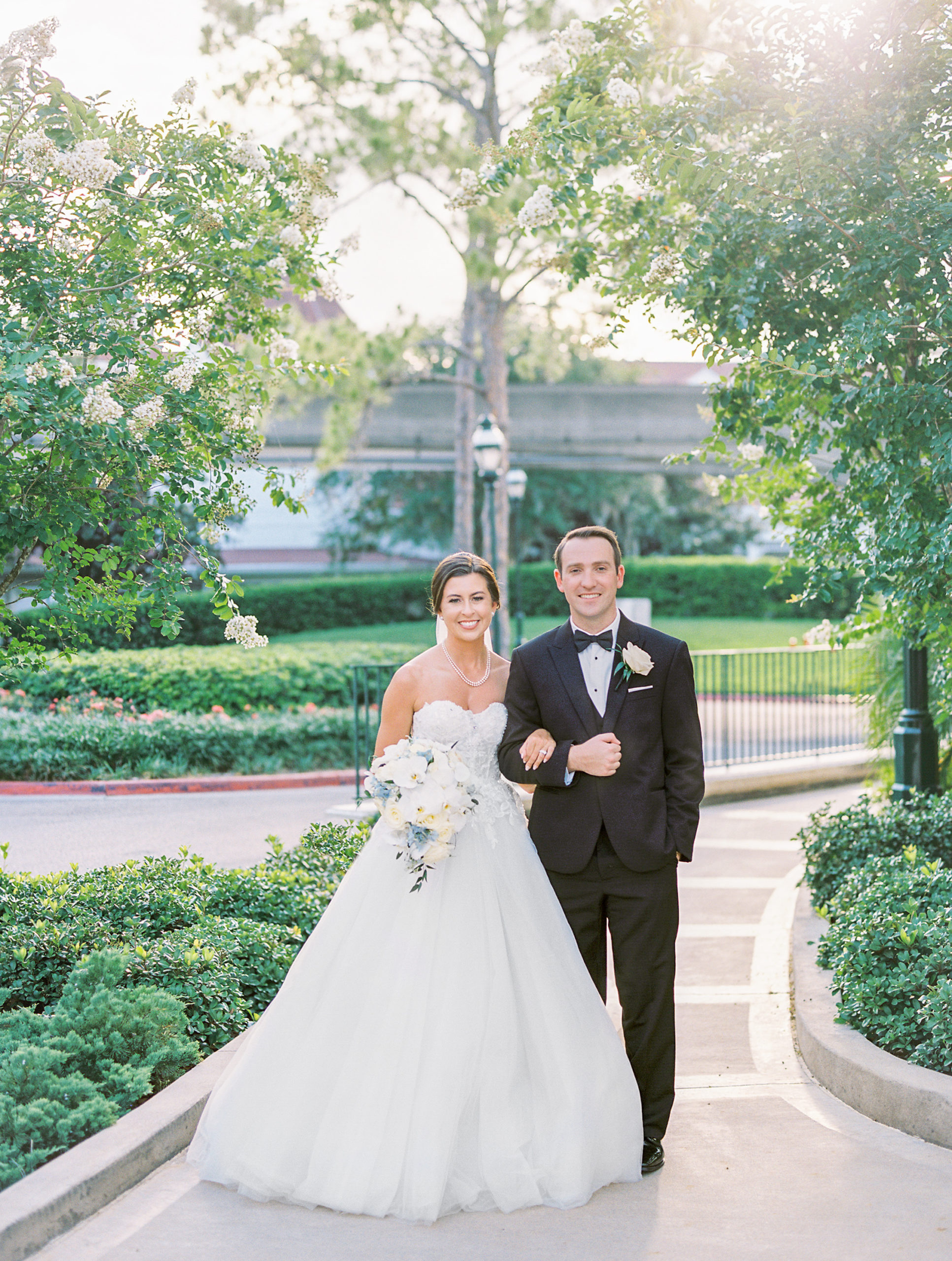 Bride and groom interlock arms and smile on pathway with tree in background at Romantic and Timeless Grand Floridian Wedding 