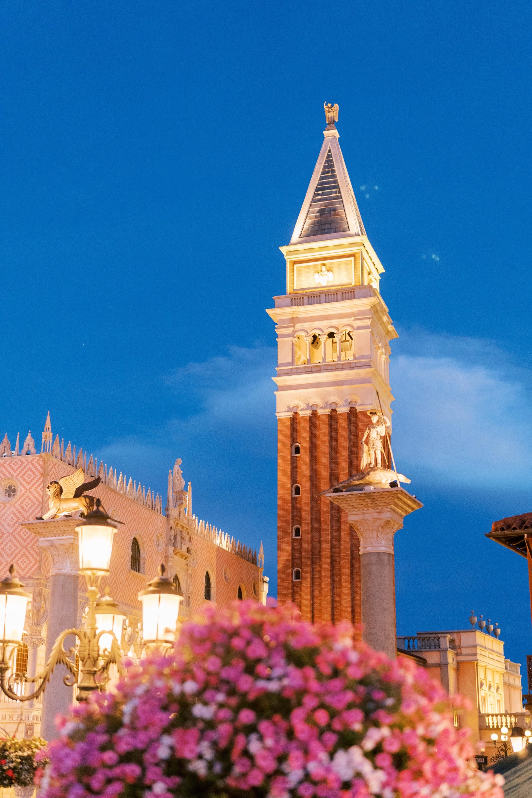 Bell tower and replica of St. Mark's Square at Disney at night with pink flowers at a Romantic and Timeless Grand Floridian Wedding 