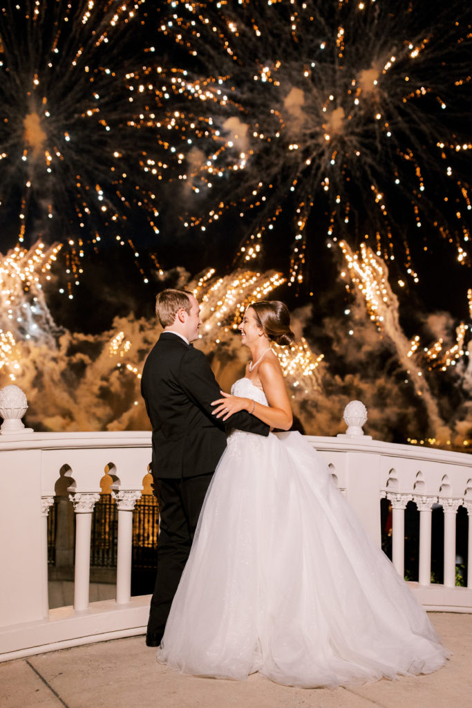 Bride and groom embrace and laugh with gold fireworks 