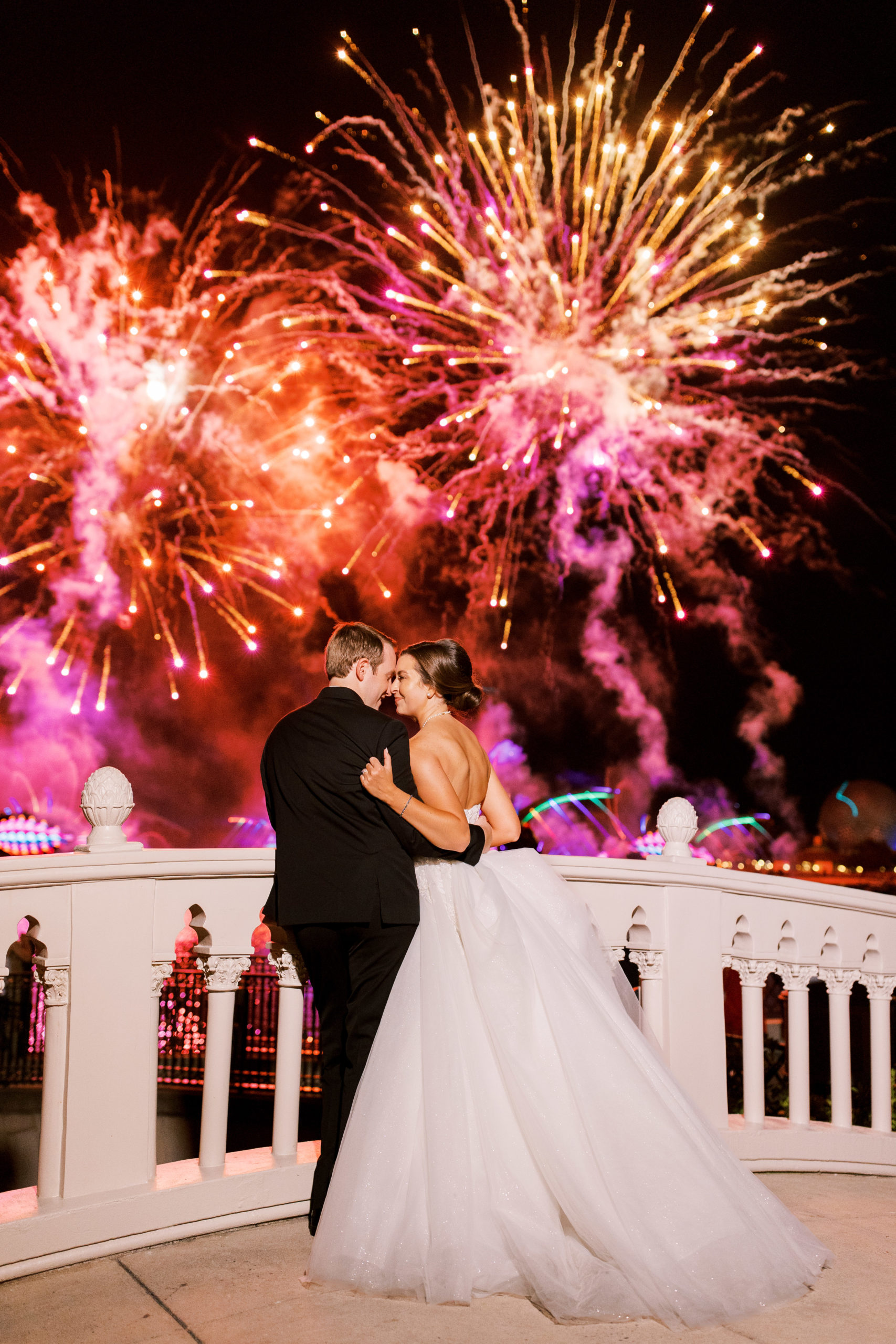 Bride and groom look into each other's eyes on bridge with orange and pink fireworks for a Romantic and Timeless Grand Floridian Wedding 