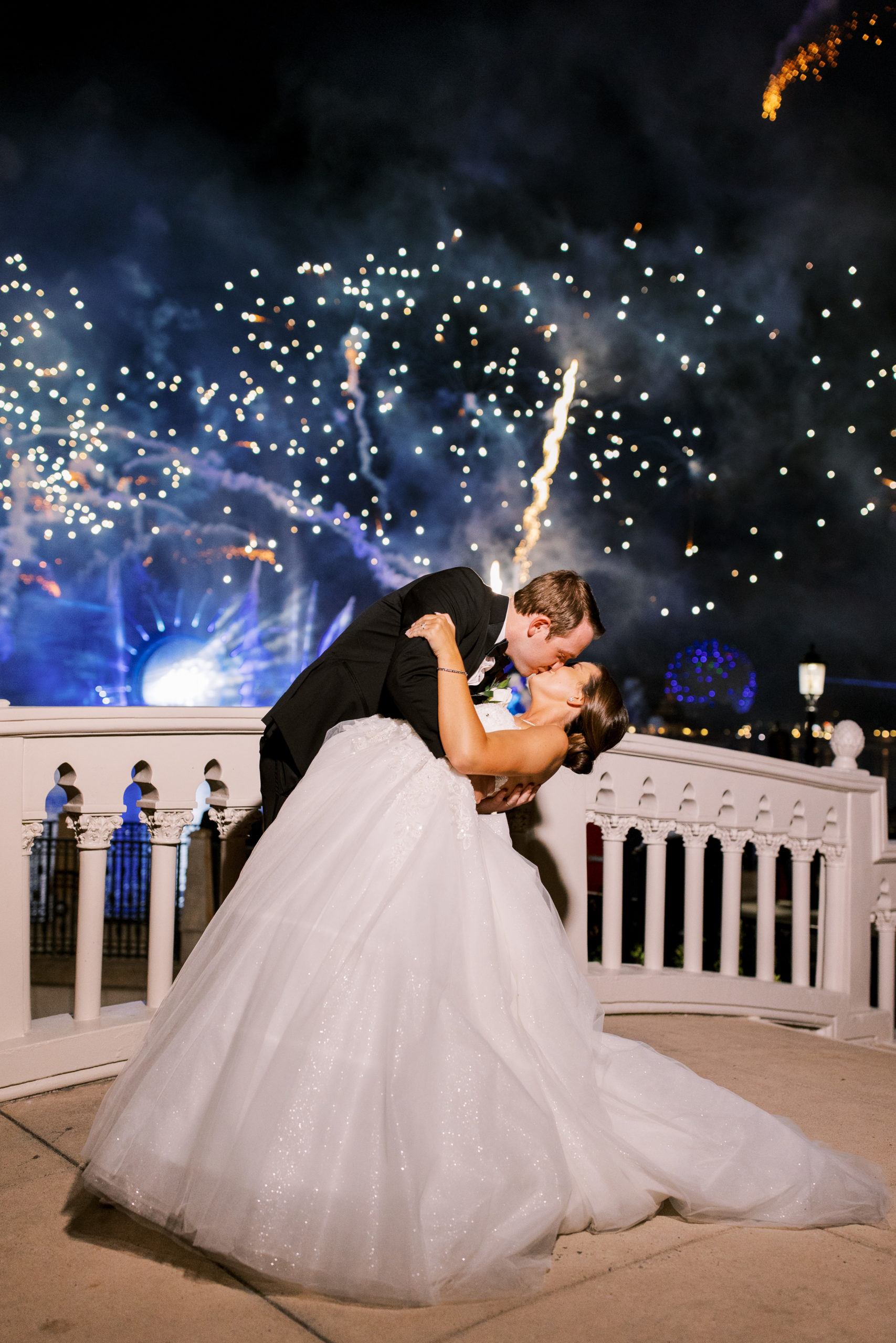 Bride and groom kiss on bridge at Disney with blue and gold fireworks at a Romantic and Timeless Grand Floridian Wedding 