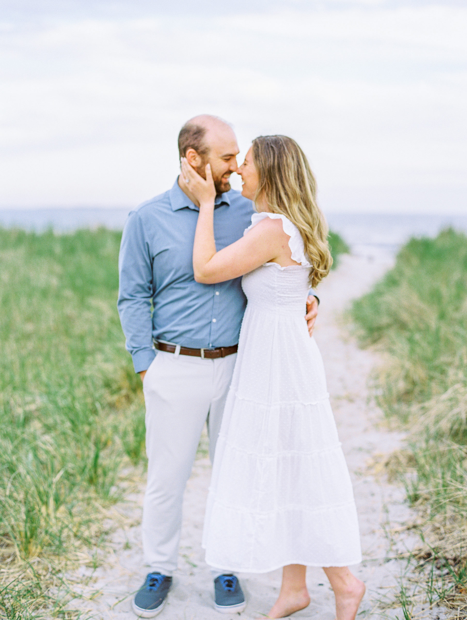 Couple laugh and hold each other on beach path at Coastal Maine Engagement Session 