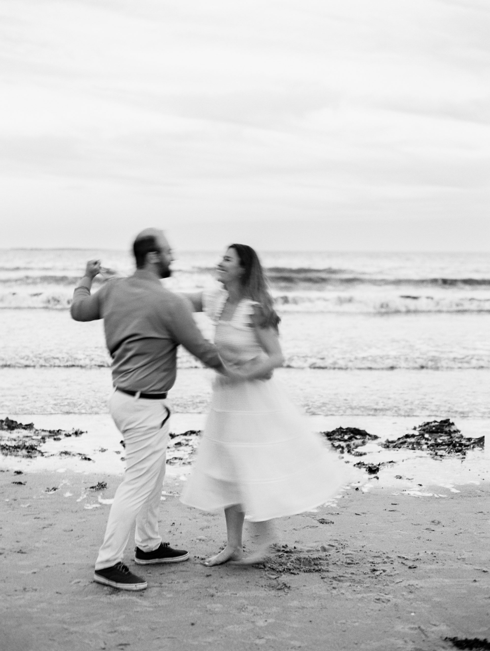 Couple smiles and dances by the ocean for Coastal Maine Engagement Session 
