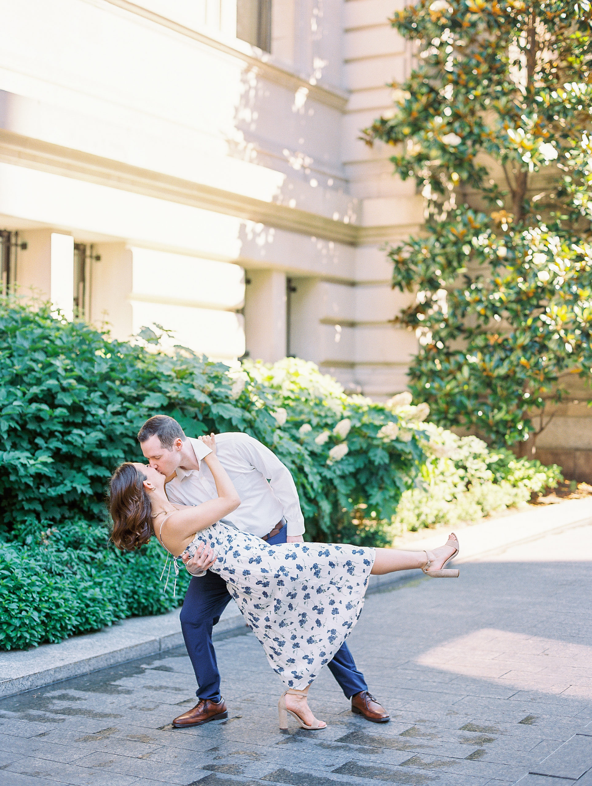 Couple dip kisses on stone path with white hydrangeas blooming for Central Park Engagement Photos