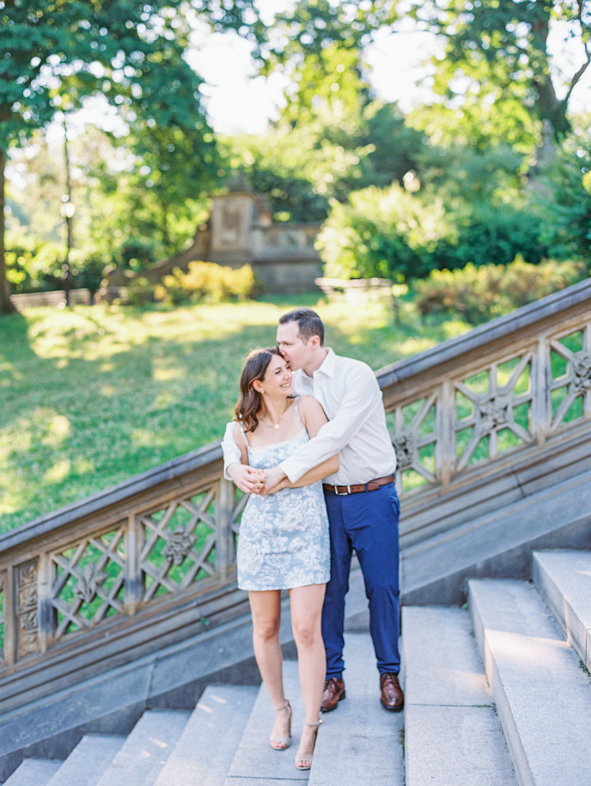 Couple embraces and gives a kiss on forehead on stone steps in Central Park for Central Park Engagement Photos
