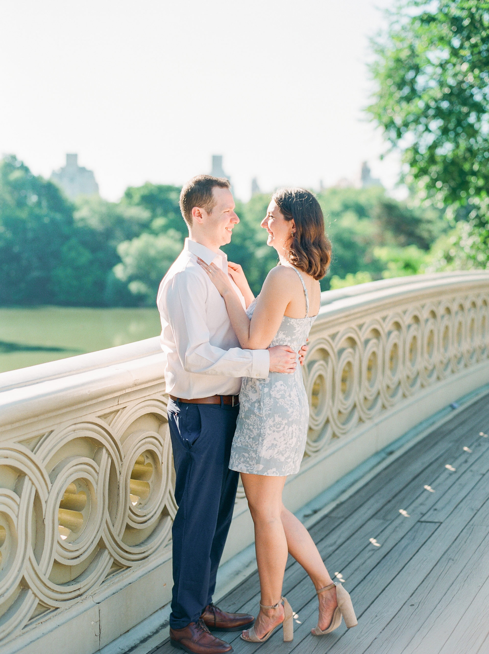 Couple smiles and embraces on top of wooden bridge in the park for Central Park Engagement Photos