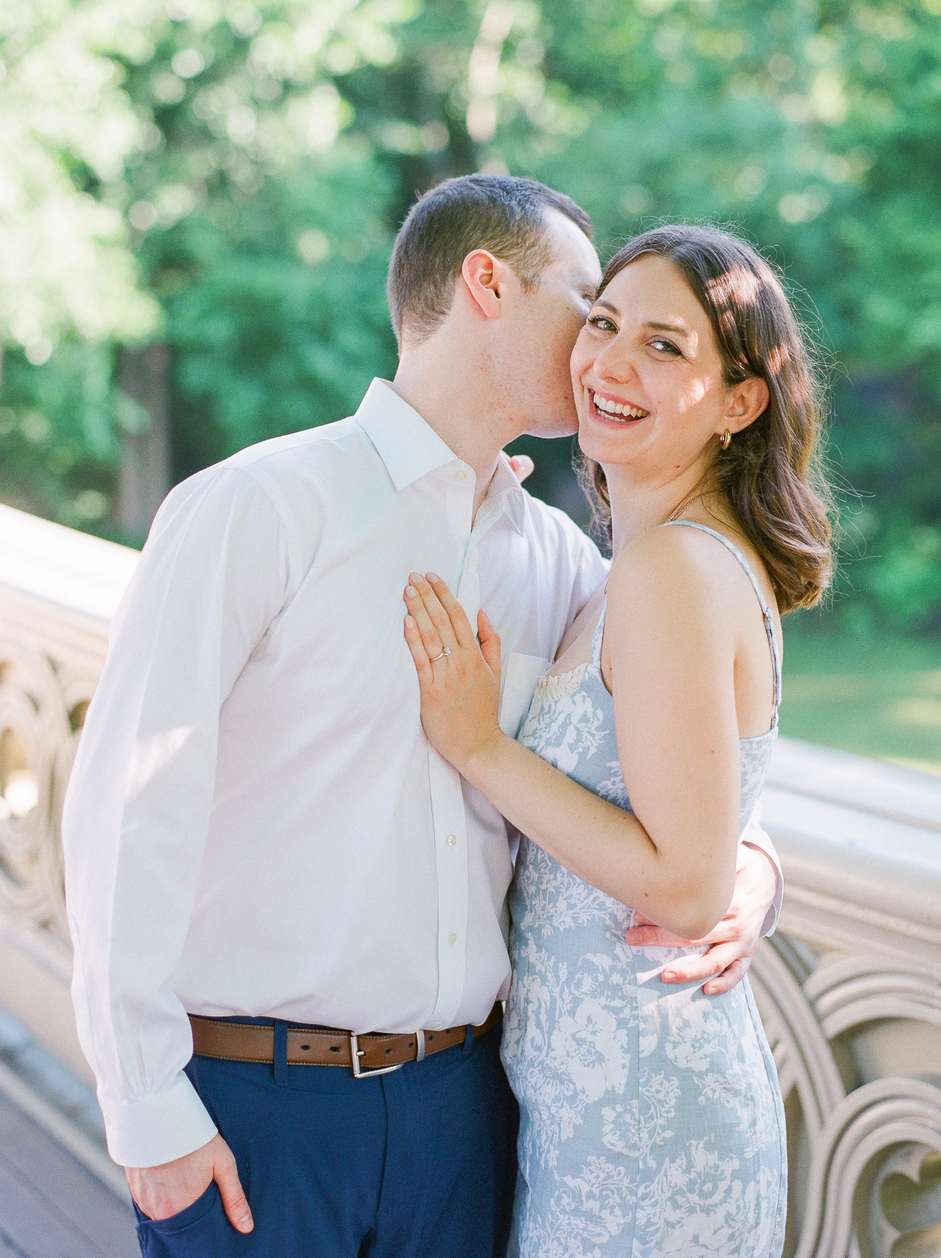 Couple embrace, smile, and whisper on bridge in the park for Central Park Engagement Photos