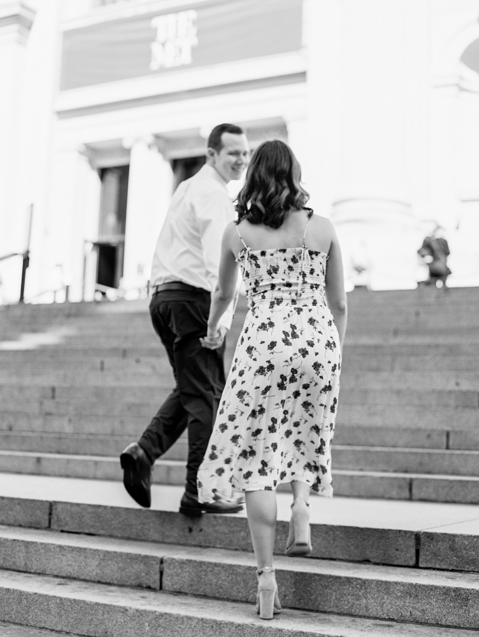 Couple holds hands and walks up stone stairs of museum 